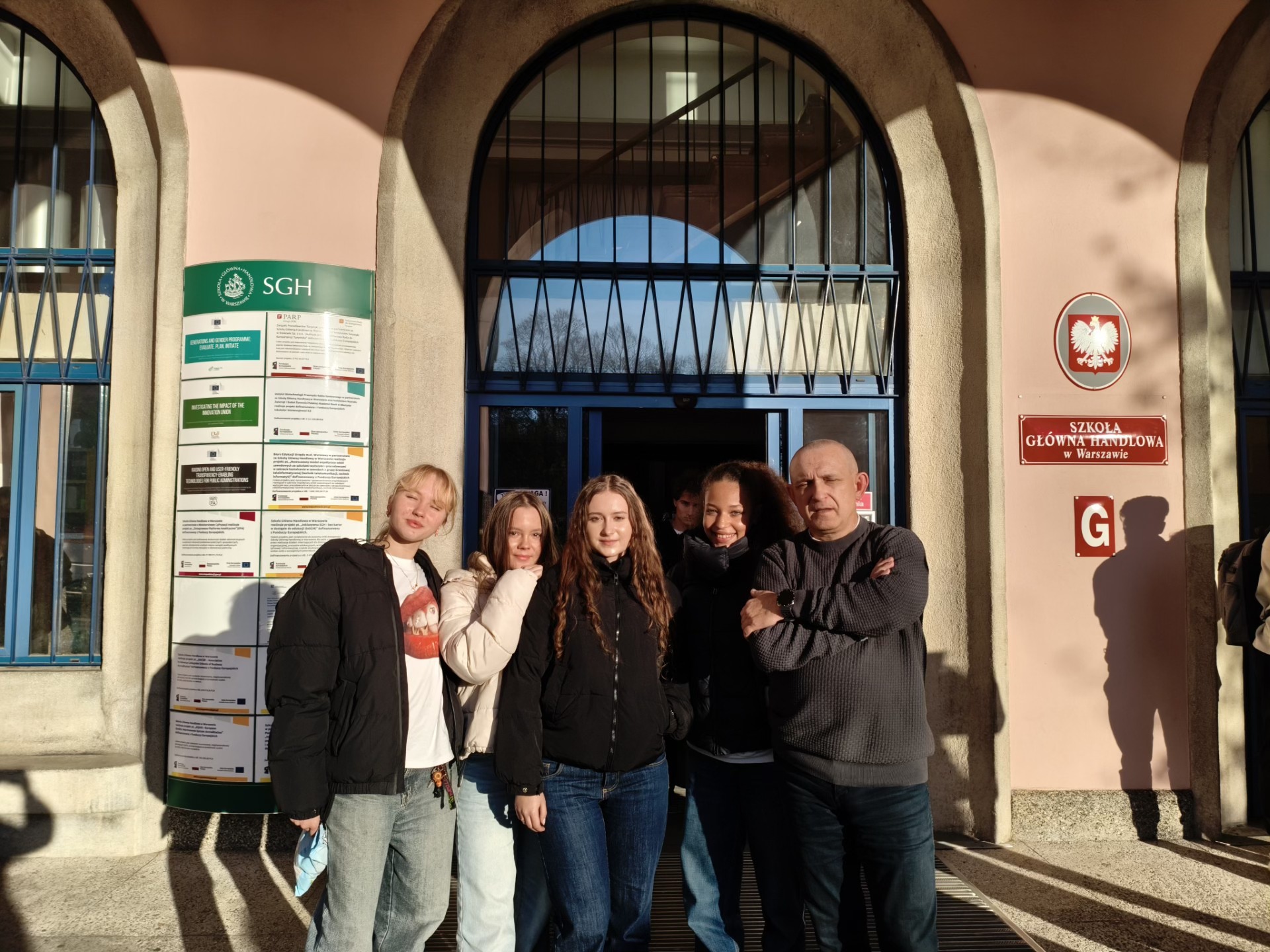 Uczennice pozują z profesorem przed budynkiem